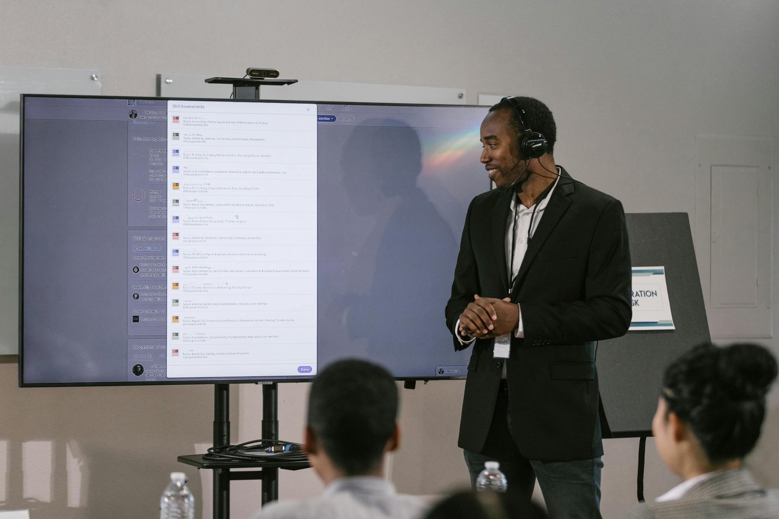 An adult man presents at a technology seminar using a large screen and headset.